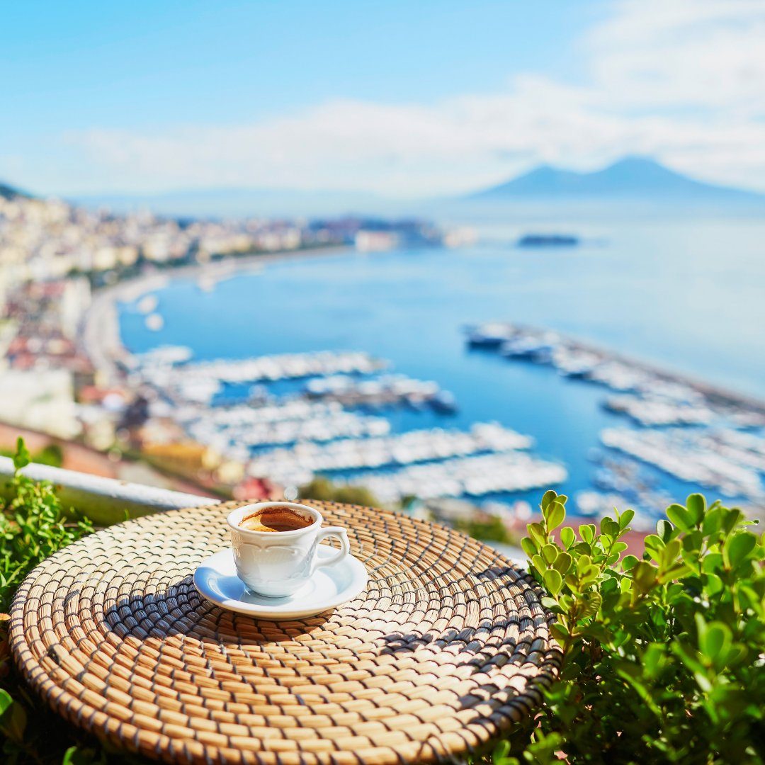 Cup of Neapolitan espresso on a woven table overlooking the Bay of Naples and Vesuvius
