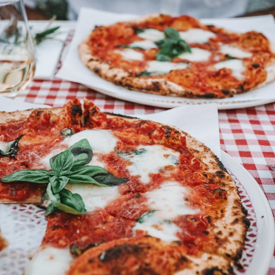 Two wood-fired Neapolitan pizza margherita with basil on a checked tablecloth